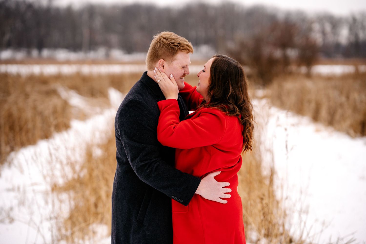 Winter engagement portrait in snowy field with warm golden light.
