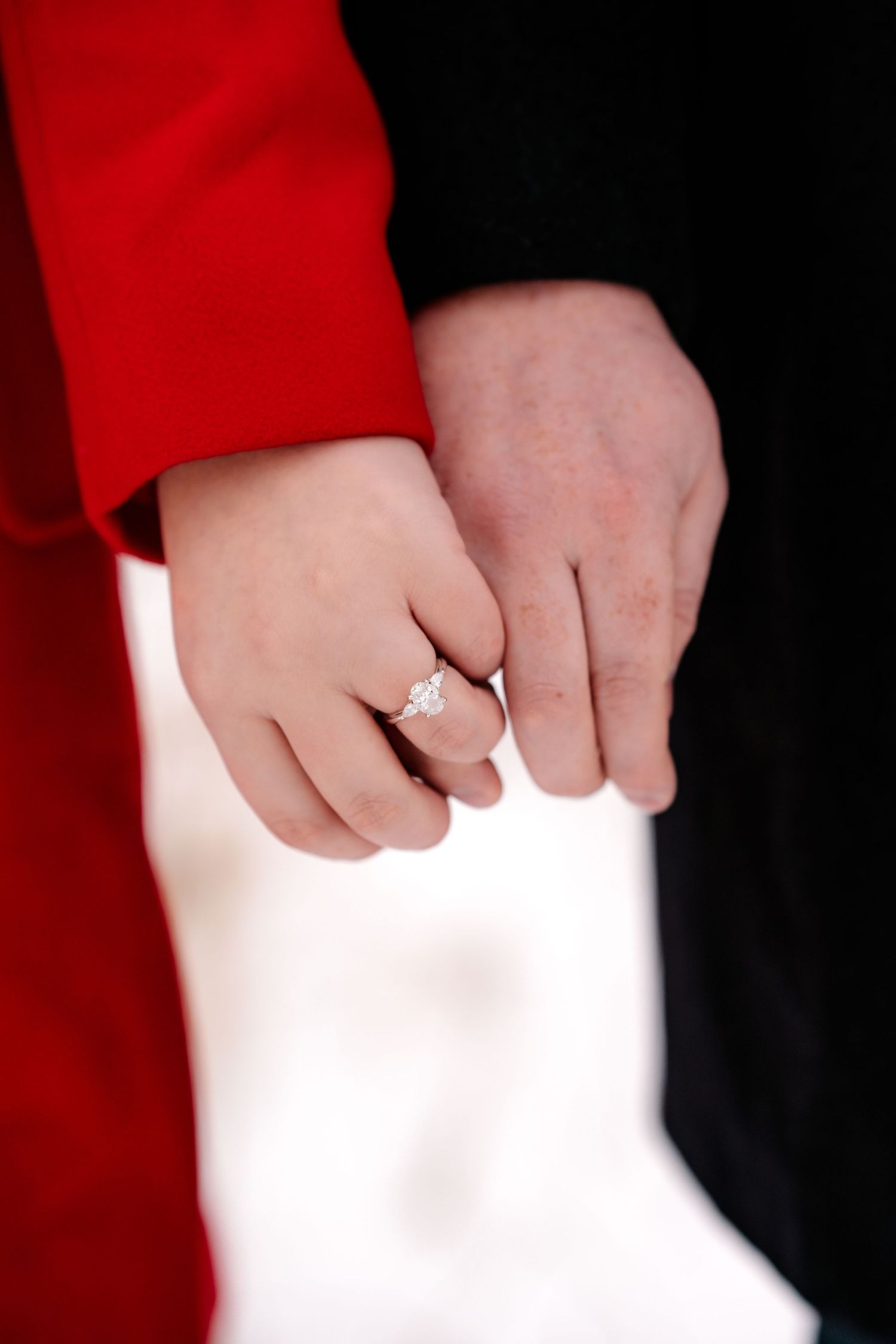 Close-up of hands showing engagement ring against red and black clothing.