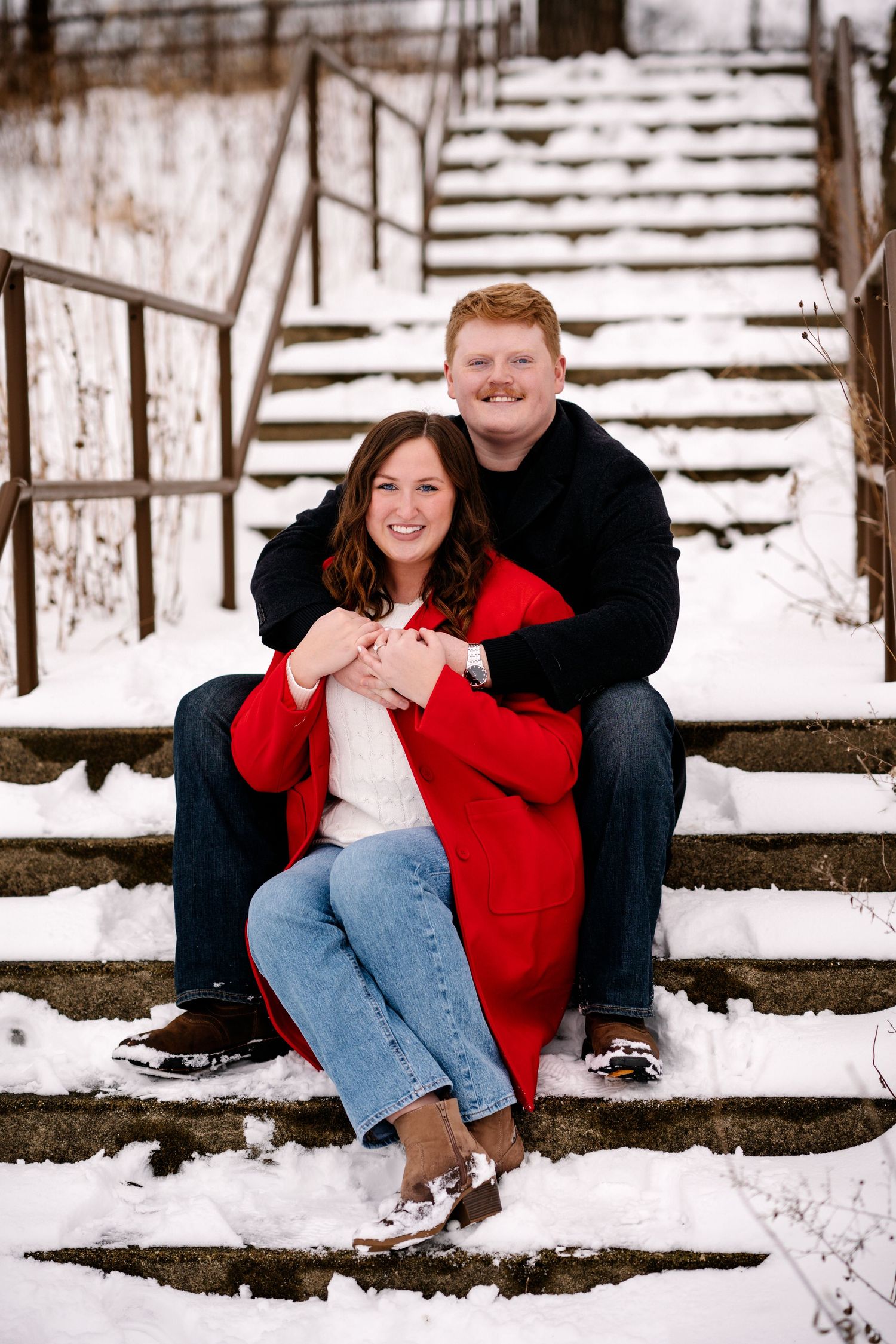 A couple sitting on snowy steps, with the woman wearing a bright red coat and the man in black.