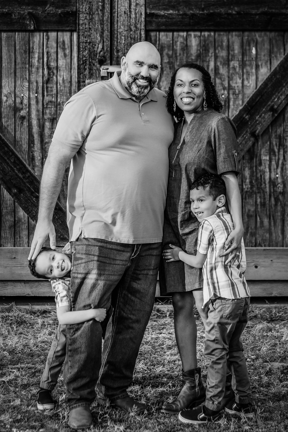 Black and white family portrait against wooden barn backdrop.