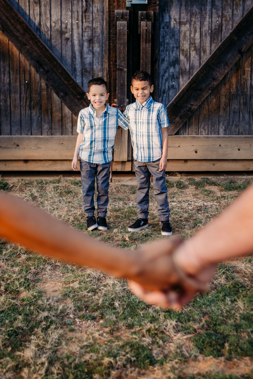 Two children in matching plaid shirts standing in front of rustic barn door.