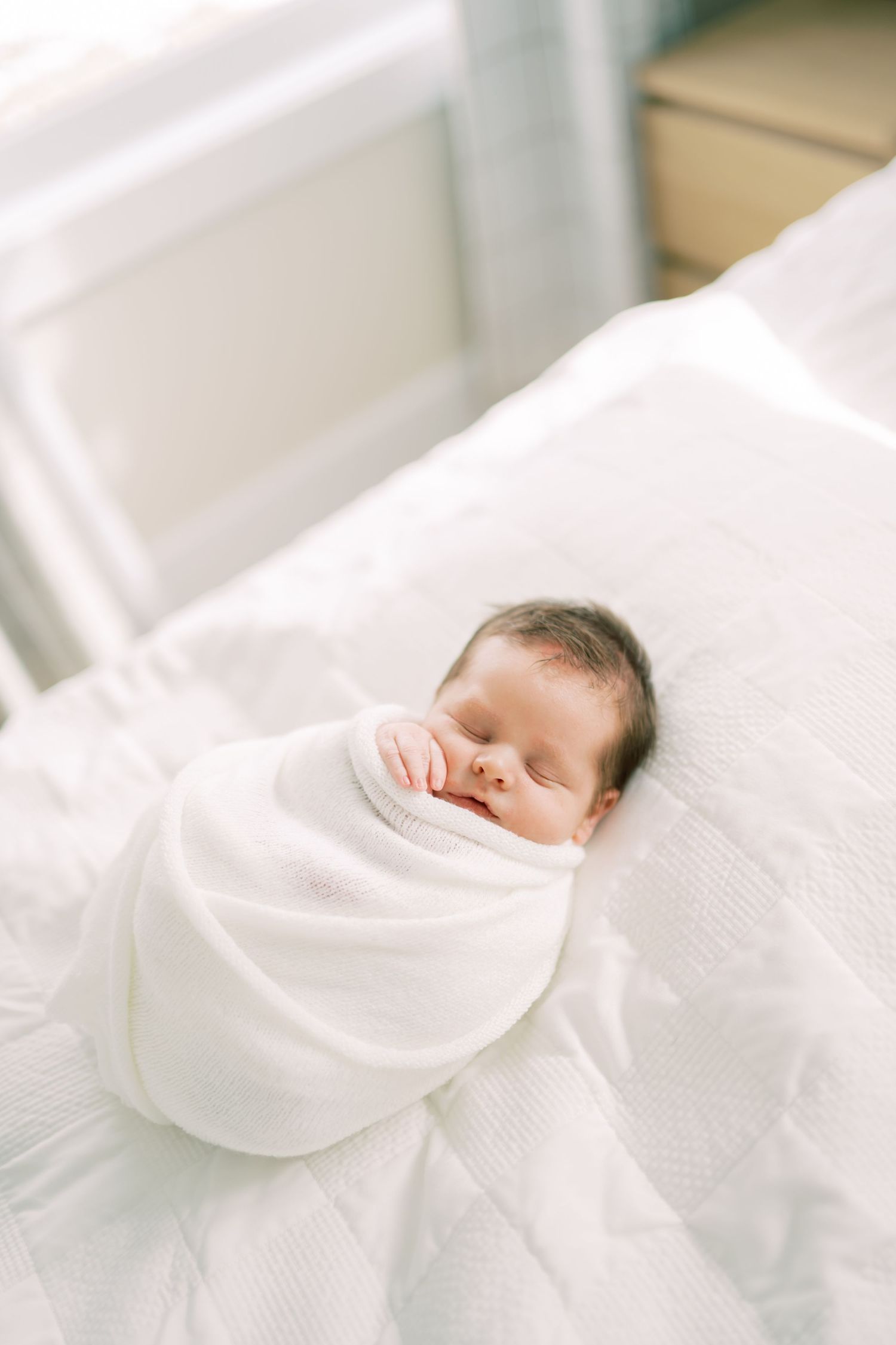 A sleeping newborn baby swaddled in soft white blankets rests peacefully on white bedding.