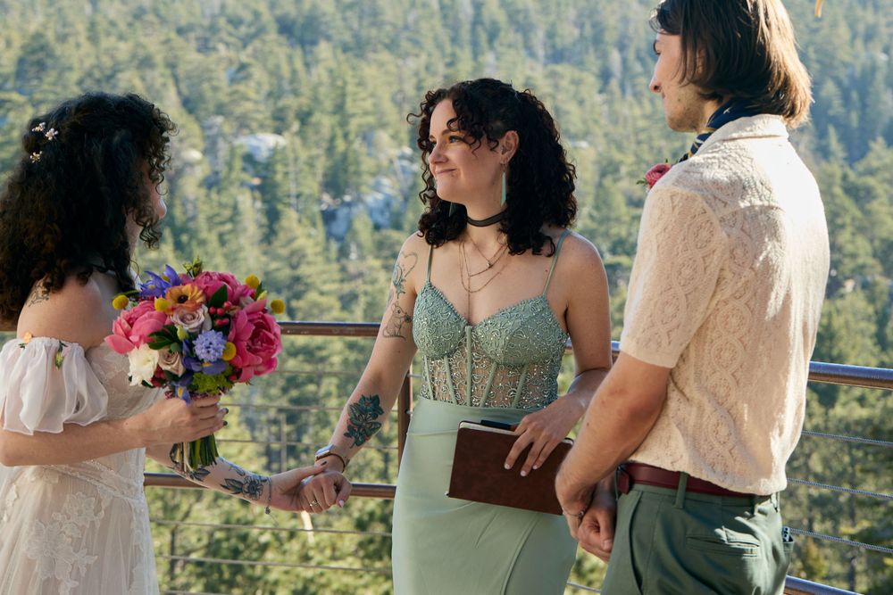 A scenic outdoor wedding ceremony takes place on a mountain overlook with colorful bouquet and soft natural lighting.