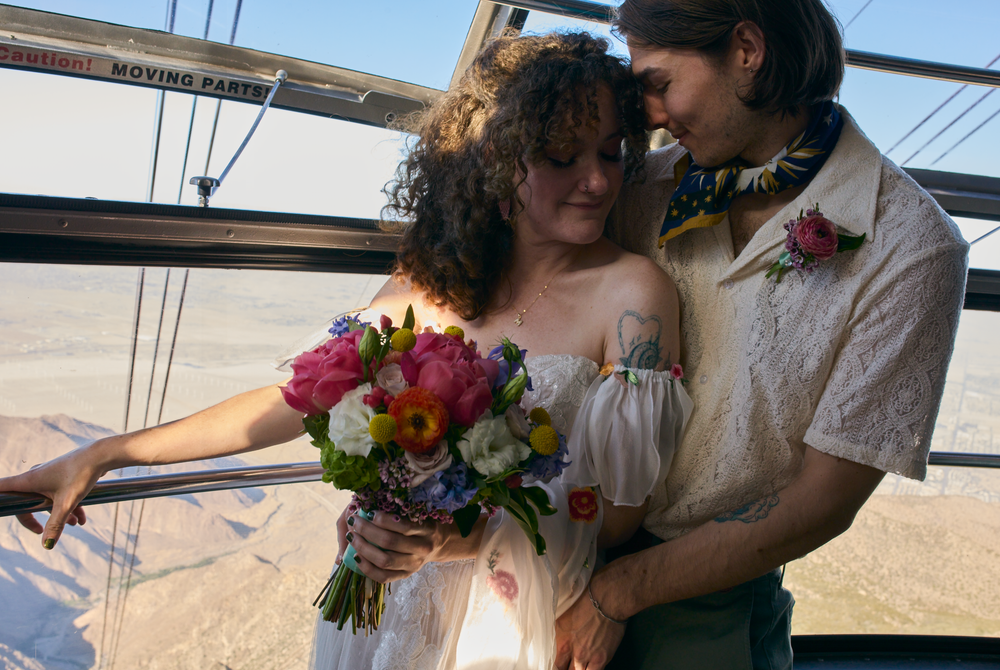 A couple share a romantic moment aboard a sailboat while holding a vibrant bouquet of flowers.