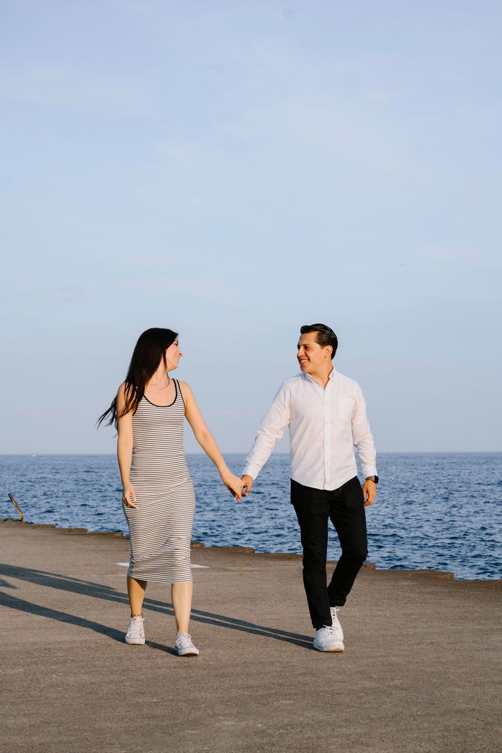 A couple holding hands while walking along the waterfront on a sunny day beside the ocean.