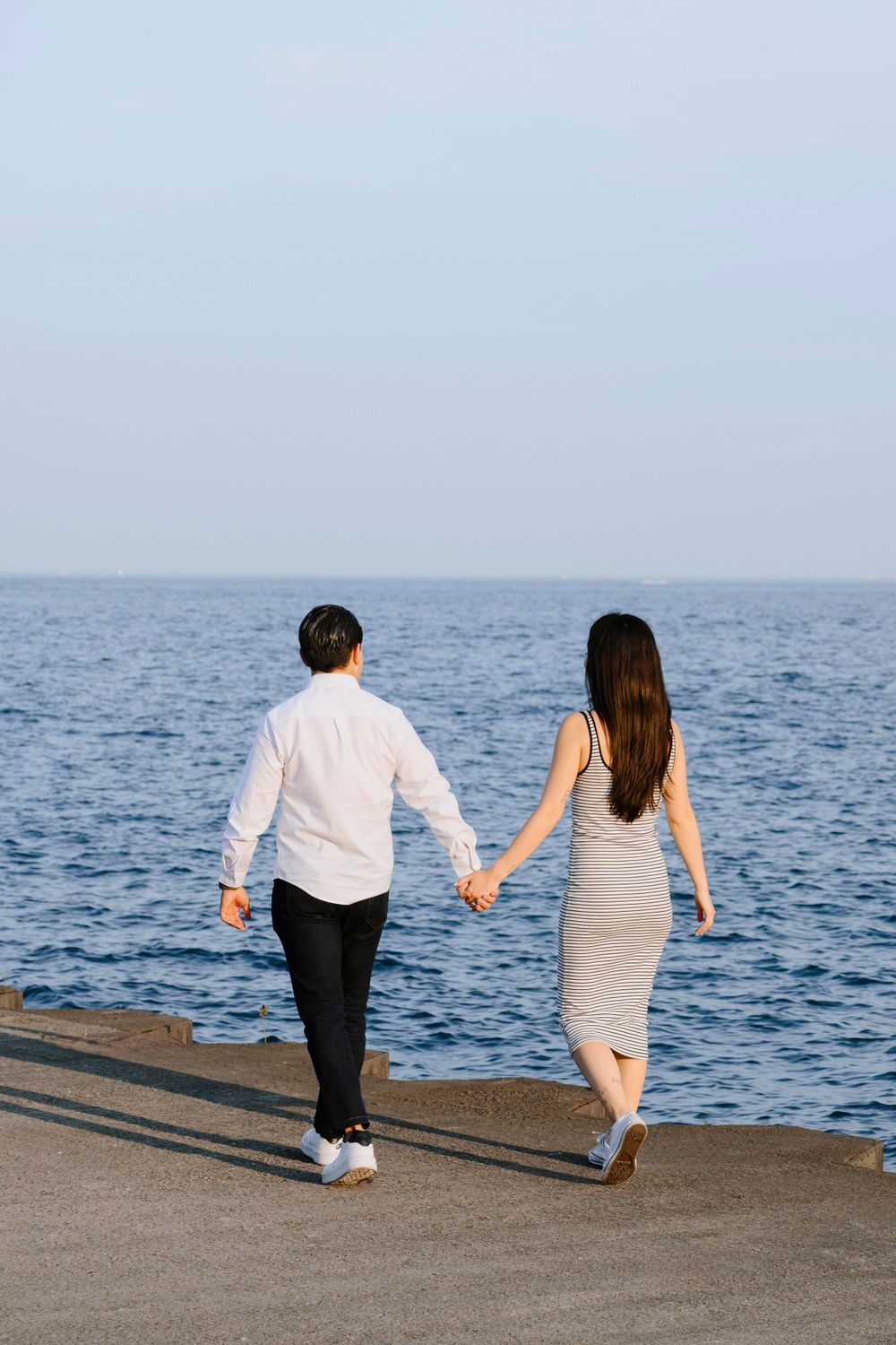 Couple walks hand in hand along waterfront path with ocean view.