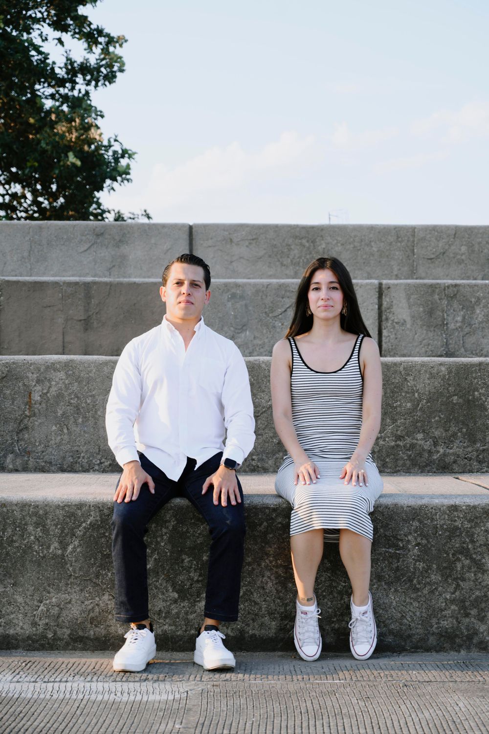Couple sits on concrete steps wearing coordinated white and striped outfits.