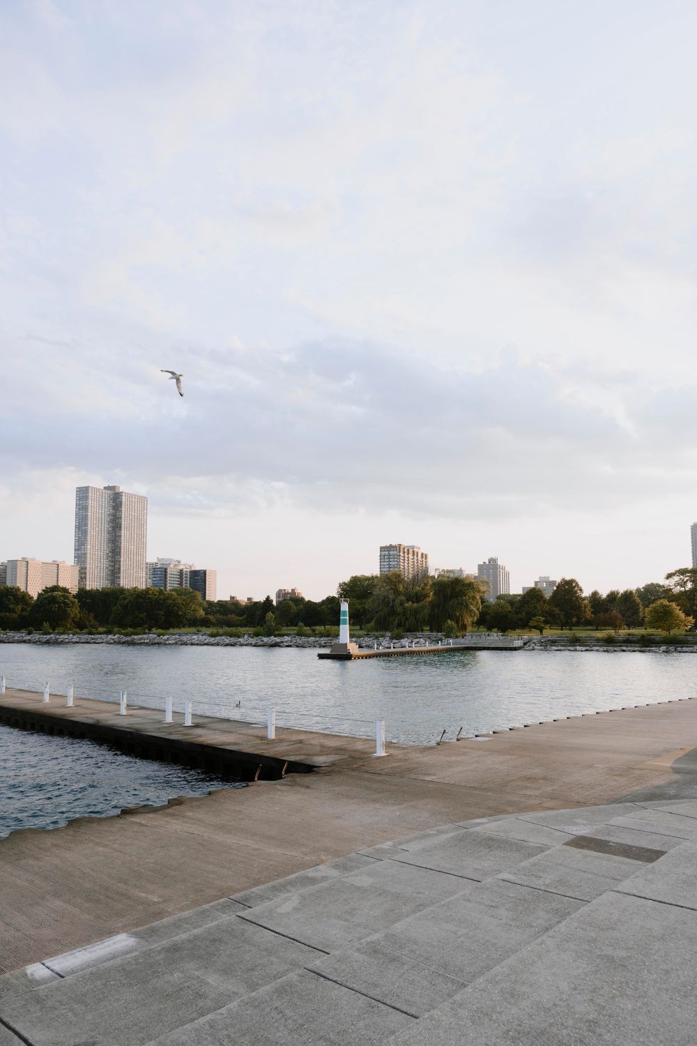 Concrete dock overlooking an urban waterfront with high-rise buildings and a lighthouse in the background.