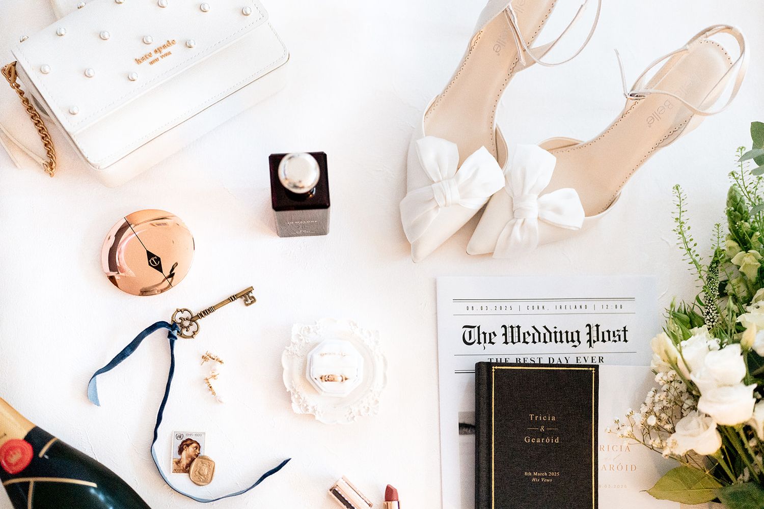 Elegant wedding accessories including white shoes, newspaper, and floral decor arranged on white surface.