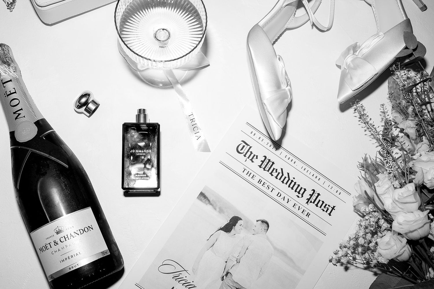 A black and white flatlay with champagne bottle, newspaper, phone and table decor arranged stylishly.