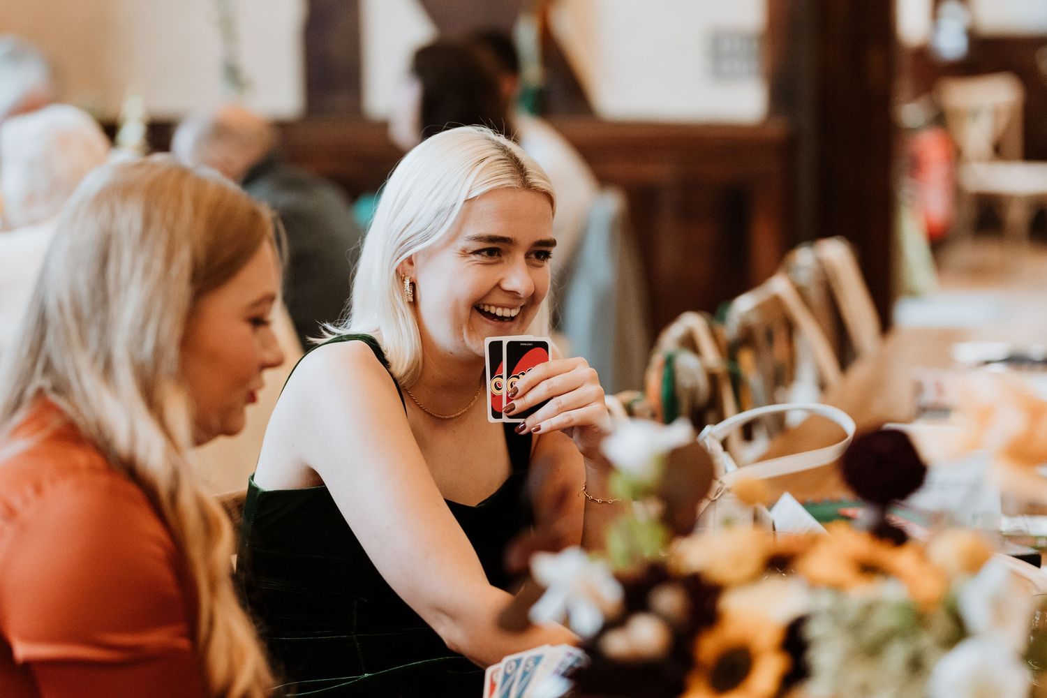 Friends enjoying drinks and uno at wedding reception gathering in warm lighting.