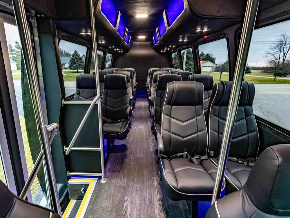 Interior view of a luxury shuttle bus with leather seats and blue accent lighting.