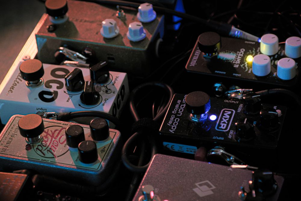 Collection of guitar effect pedals illuminated with dramatic colored lighting.