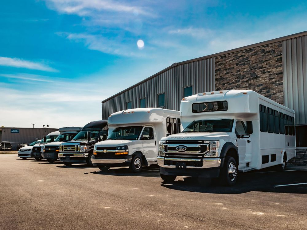 Fleet of commercial transport vehicles lined up outside a building with stone and metal siding.