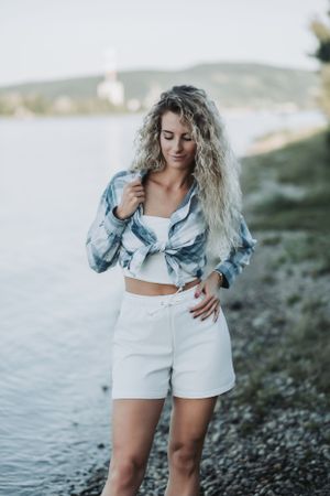 Woman in tie-dye shirt and white shorts standing by waterfront.