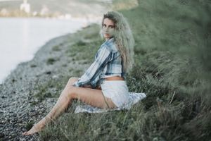 Woman in casual attire sitting on rocky shore with water view.