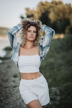 Woman in plaid shirt and white outfit posing outdoors at sunset.