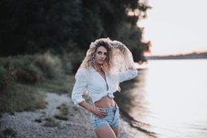 Beachside portrait of woman in casual white shirt and shorts during golden hour.
