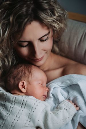Tender moment between mother and newborn wrapped in white blanket.