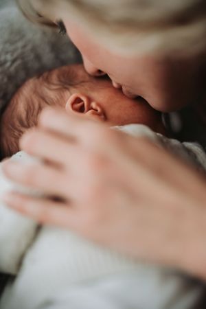 Close-up tender moment between parent and newborn baby with soft focus and gentle lighting.