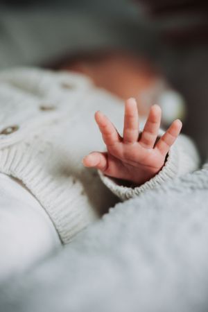 Tiny baby hand reaching up against white knitted fabric background.