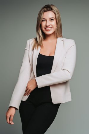 Fashion portrait of woman in cream blazer and black dress against grey backdrop.
