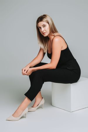 Professional modeling shot of woman in black outfit sitting on white cube.