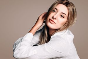 Studio beauty portrait of woman in white shirt against neutral backdrop.