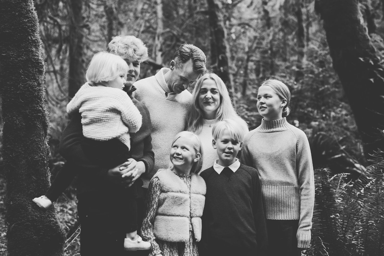 A black and white photograph showing a family of seven enjoying time together in a wooded outdoor setting.