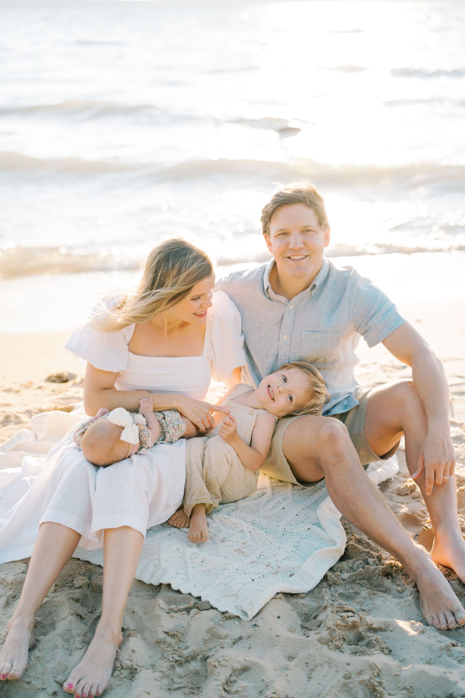 Family relaxing together on beach blanket during golden hour sunset.