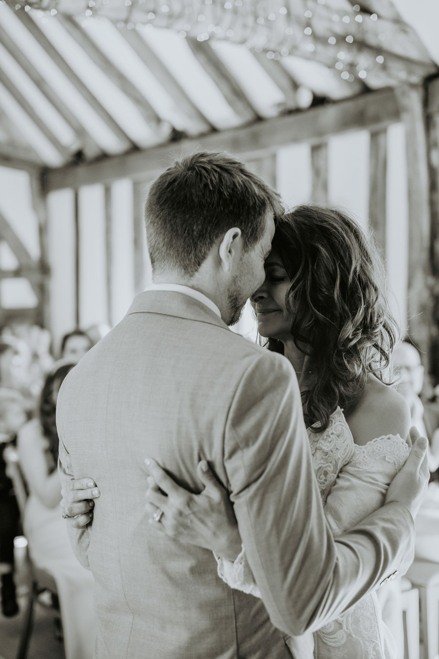 A romantic black and white photo of a newlywed couple embracing during their first dance at their wedding reception.