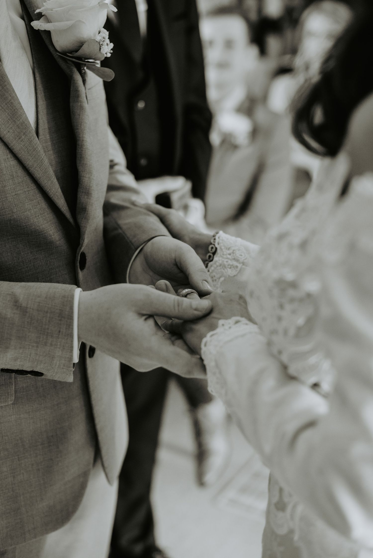 Black and white close-up photo of hands exchanging rings during an elegant wedding ceremony.