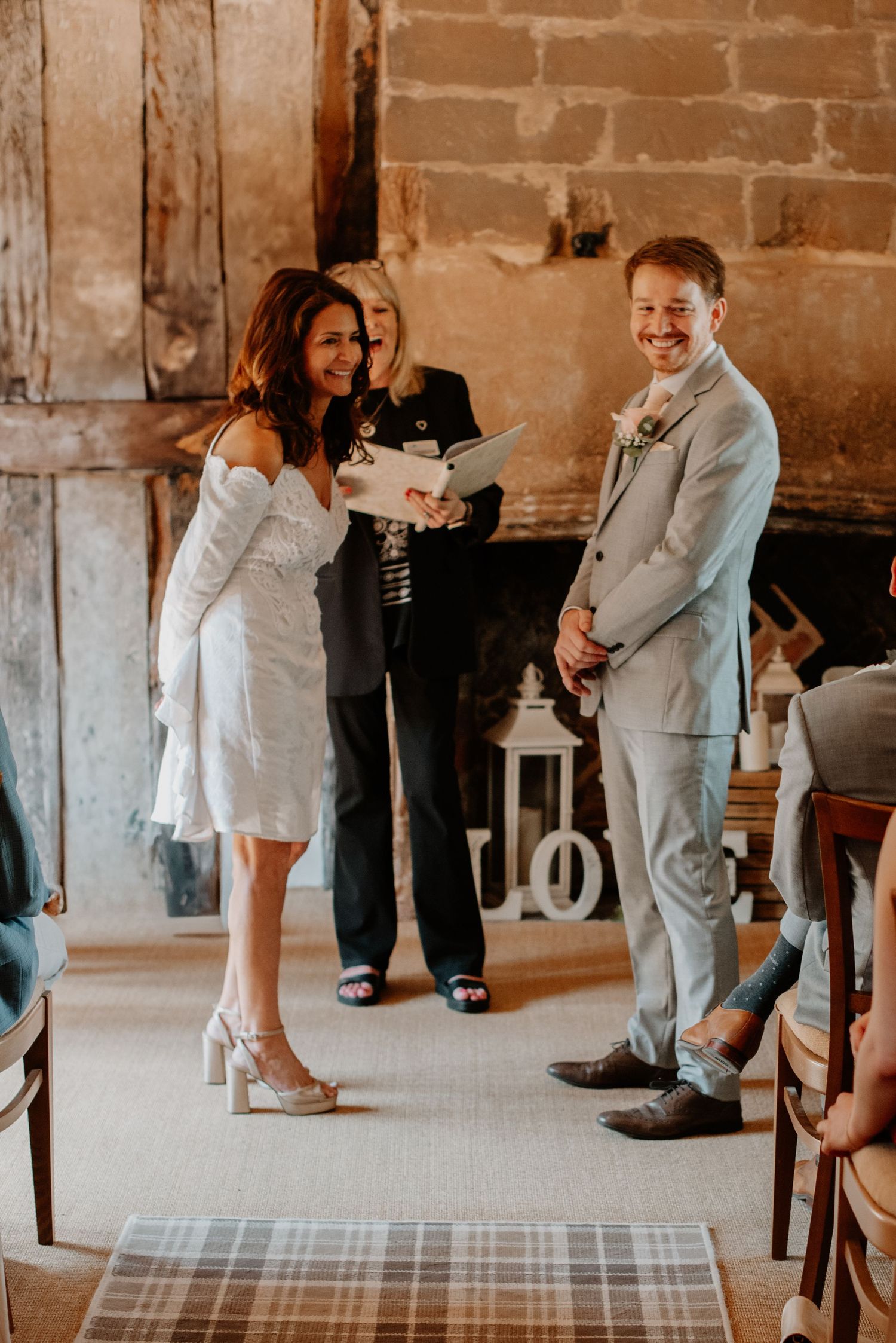 Wedding ceremony takes place in a rustic barn venue with brick walls and plaid runner on the floor.
