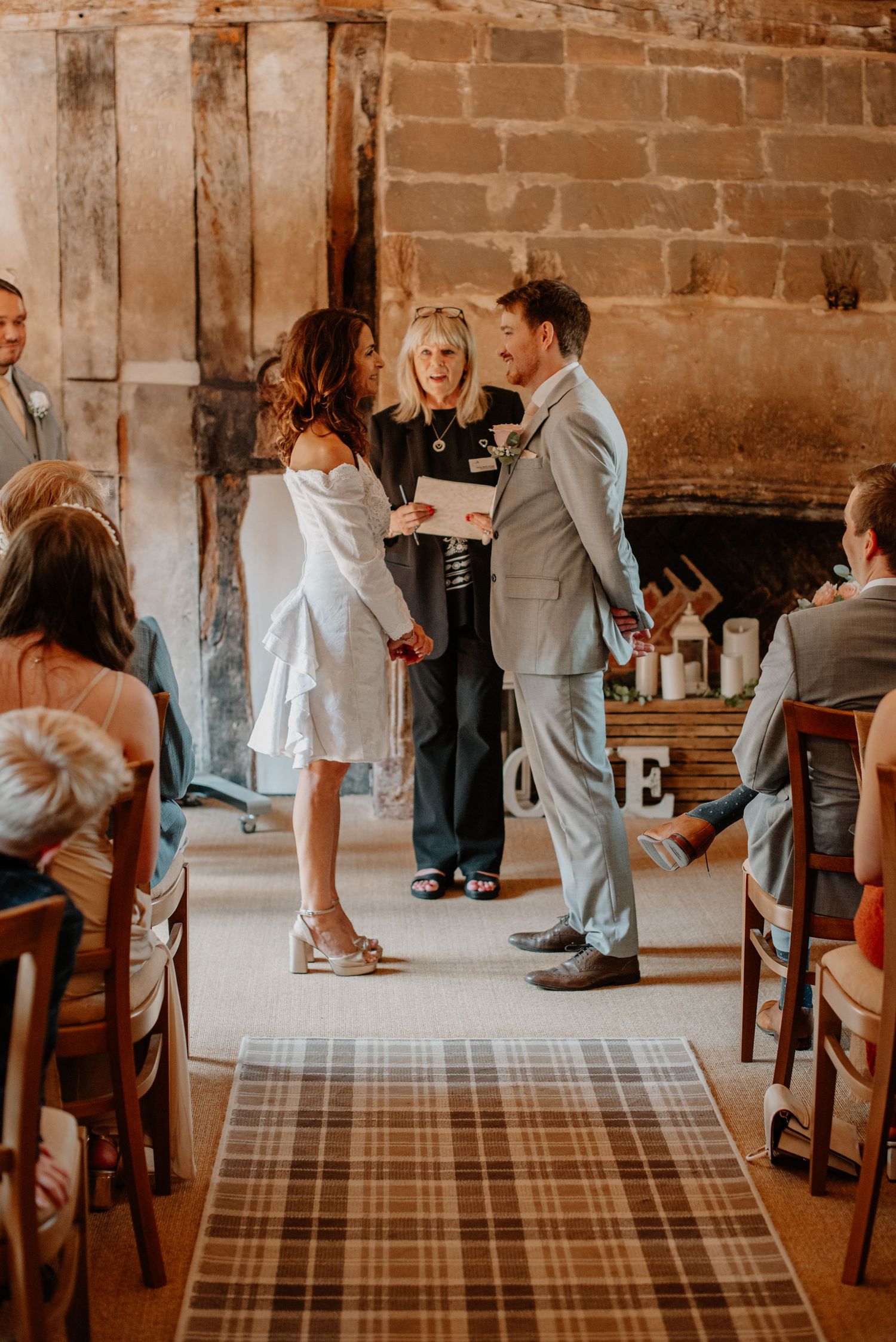 An intimate wedding ceremony takes place in a rustic stone room with a plaid runner and wooden chairs.