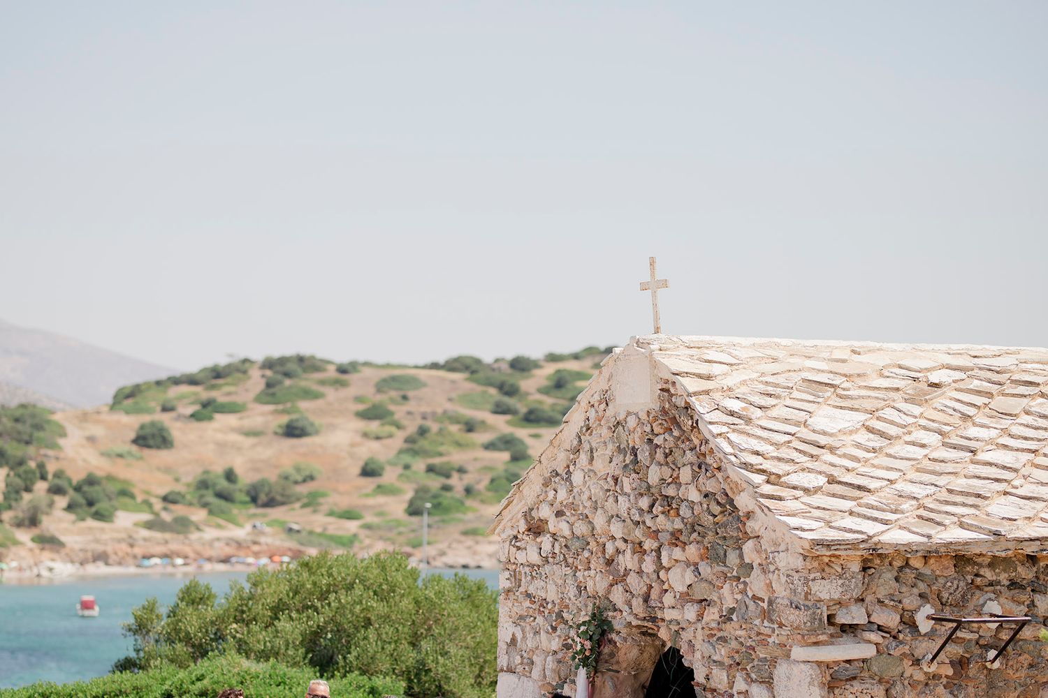 Old stone chapel with thatched roof overlooking Mediterranean coastal landscape on sunny day.