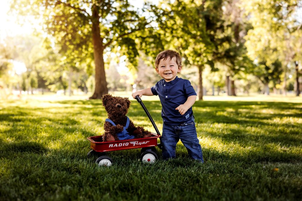 A happy child plays in a lush green field on a sunny autumn day with trees in the background. Pueblo Photographer