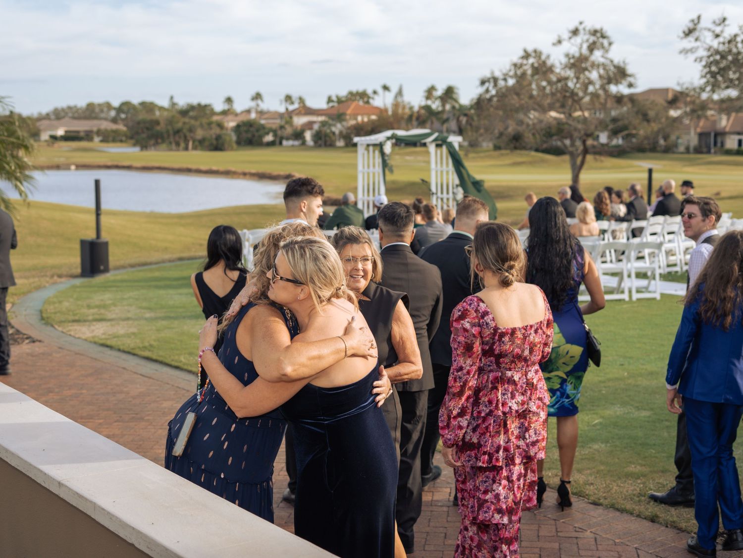 Wedding guests mingling and embracing on a golf course with water views.