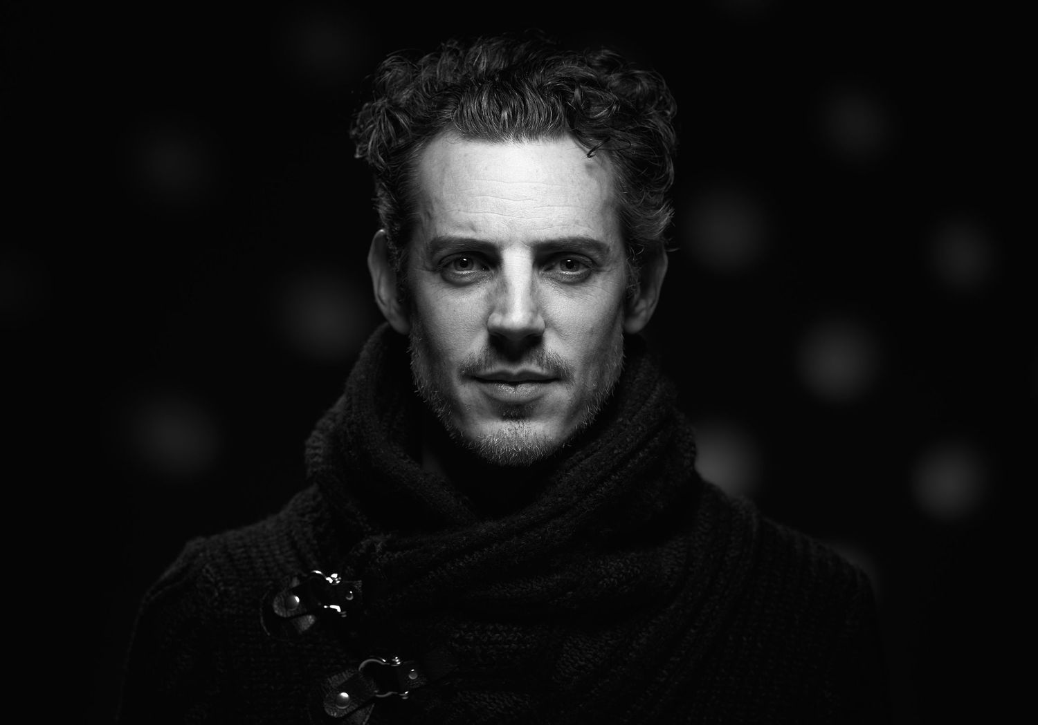 A dramatic black and white portrait of a person wearing a dark scarf in moody lighting with intense gaze.