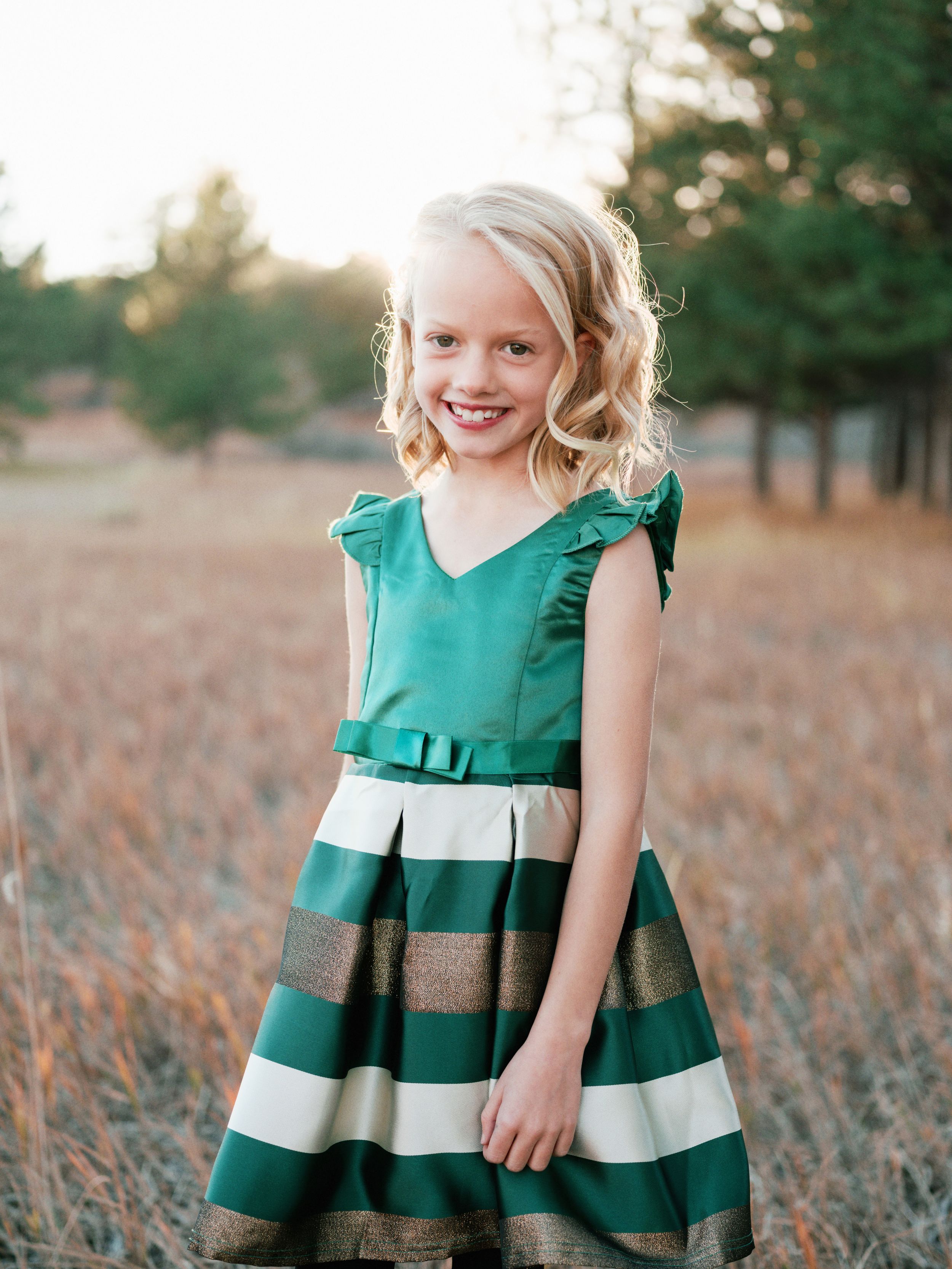 Young girl in green and white striped dress posing in autumn field.