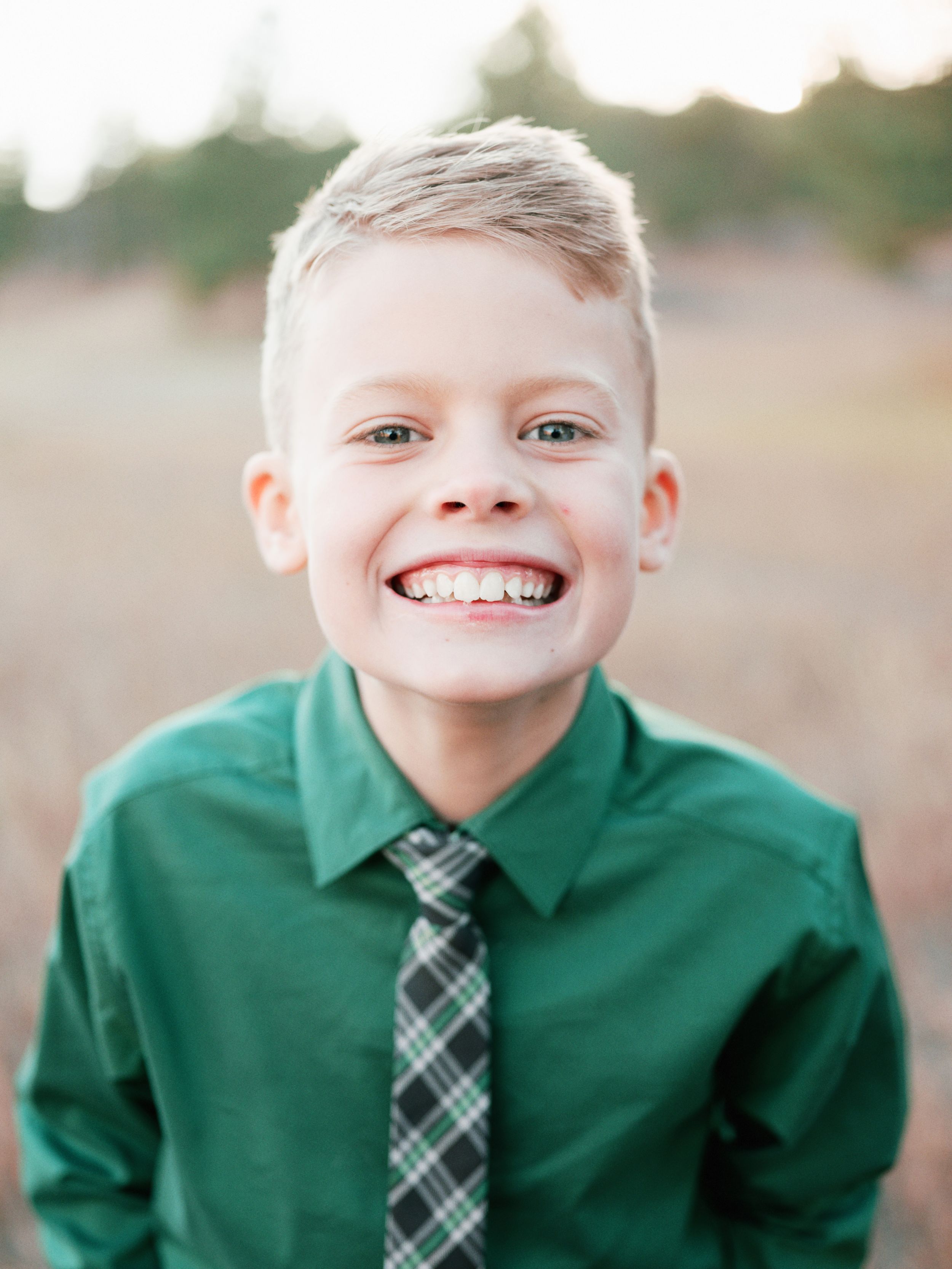 Close up portrait of child wearing green shirt and plaid tie with bright smile.