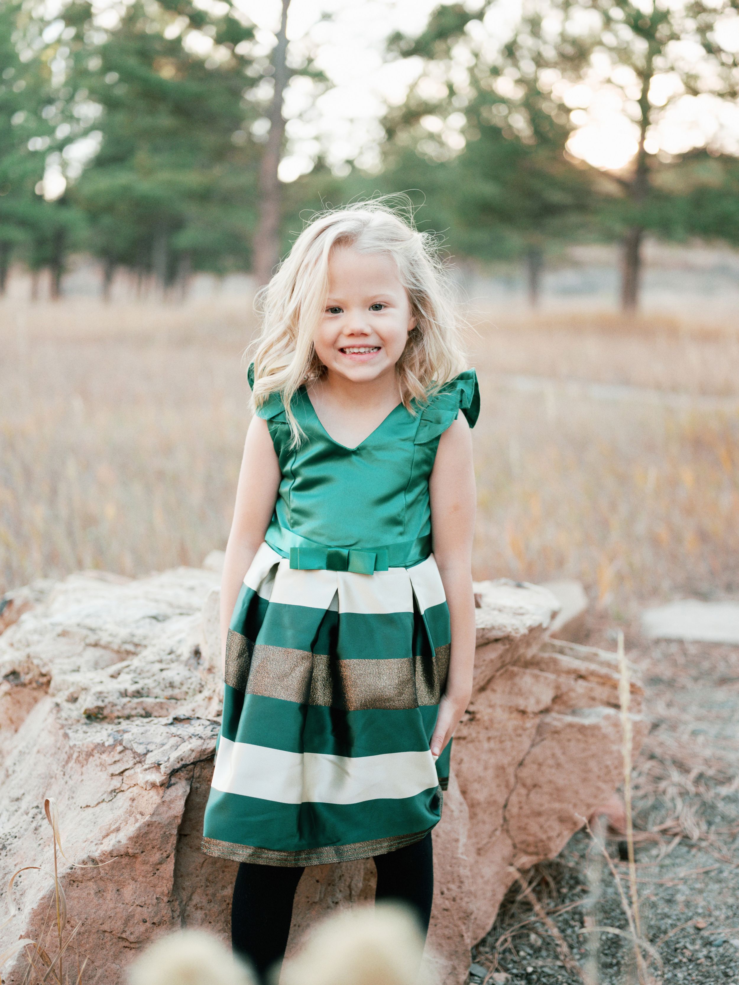 Child wearing green and white striped dress standing on rock in outdoor setting.
