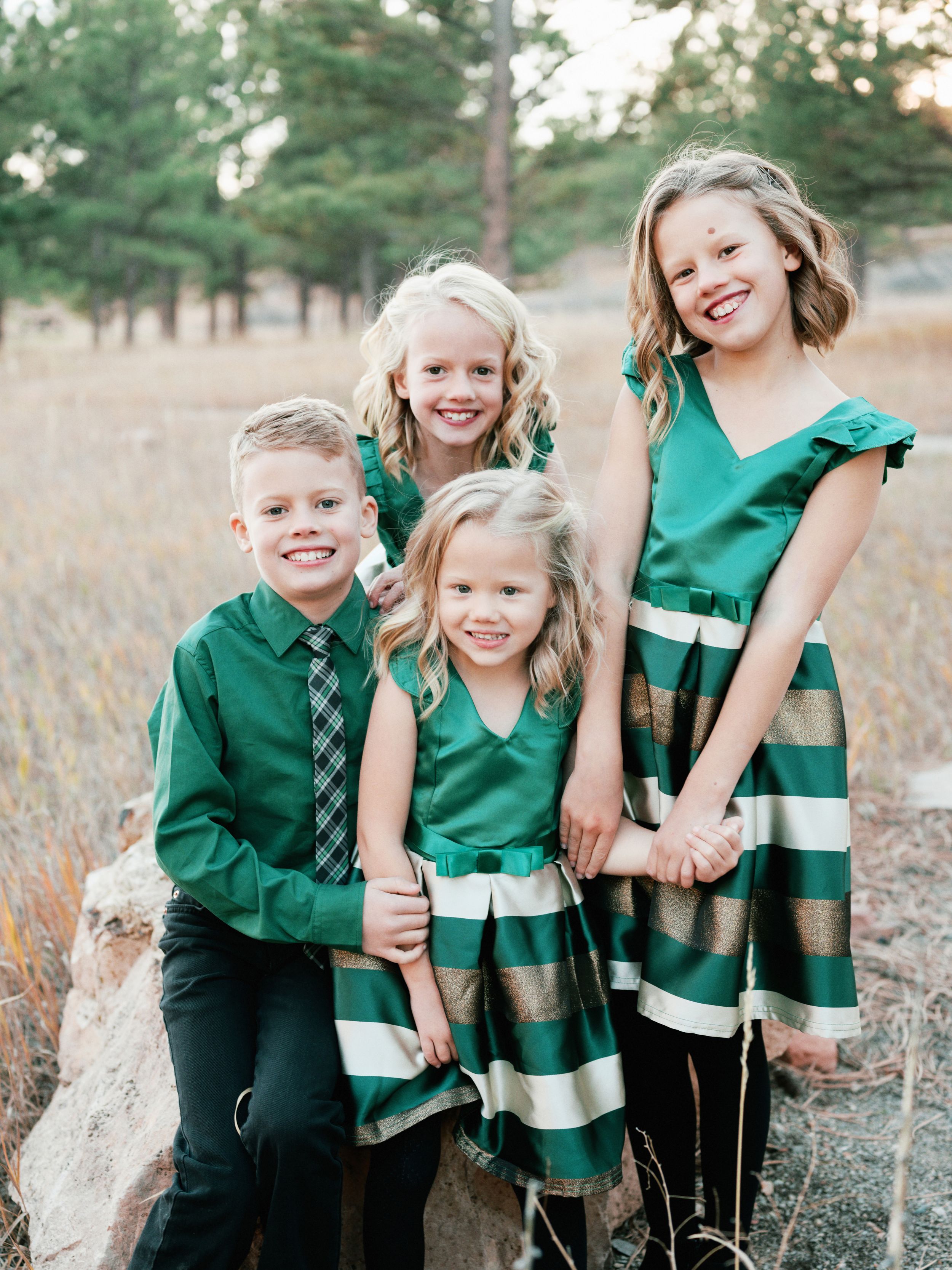 Four people in coordinating green outfits pose together on rock in outdoor setting.