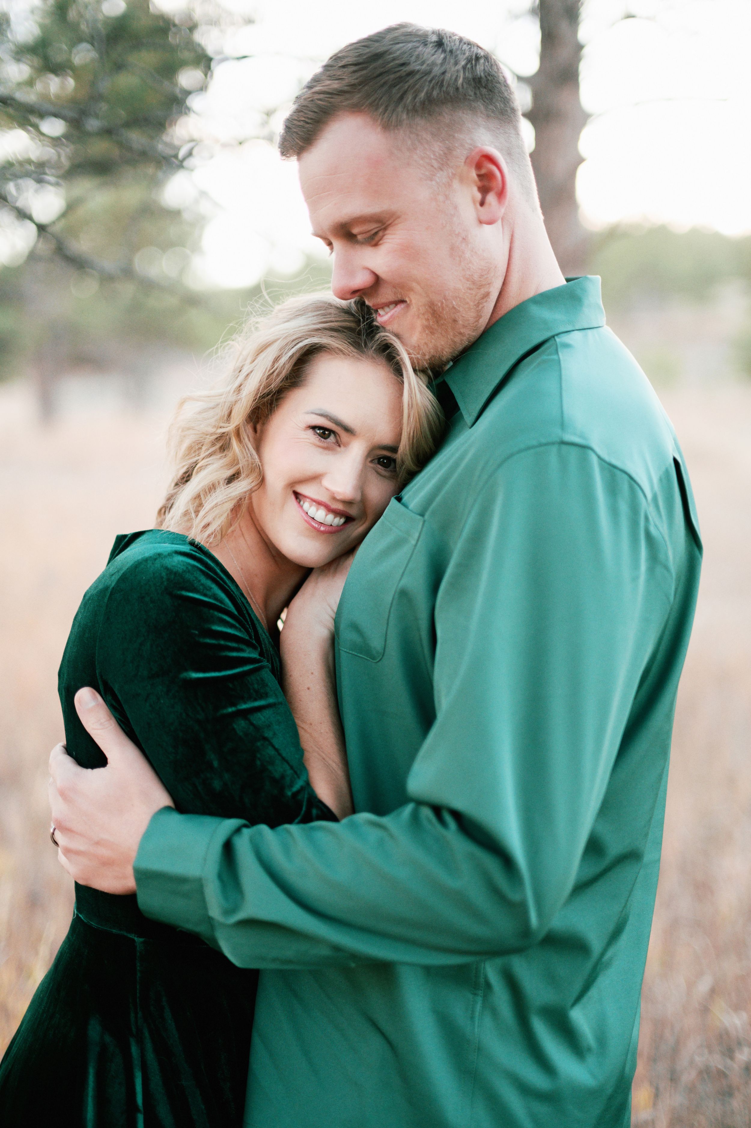 Intimate portrait of couple in green and velvet embracing outdoors.