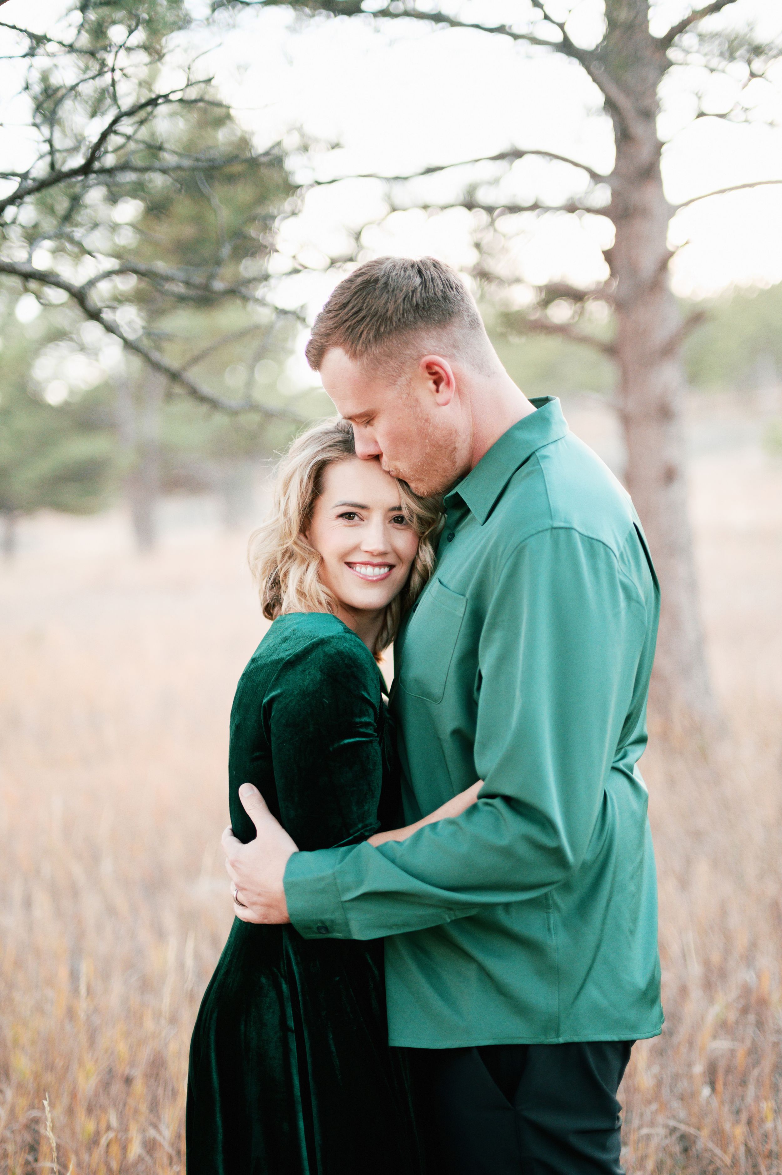 Romantic portrait of couple in green and velvet sharing tender moment outdoors.