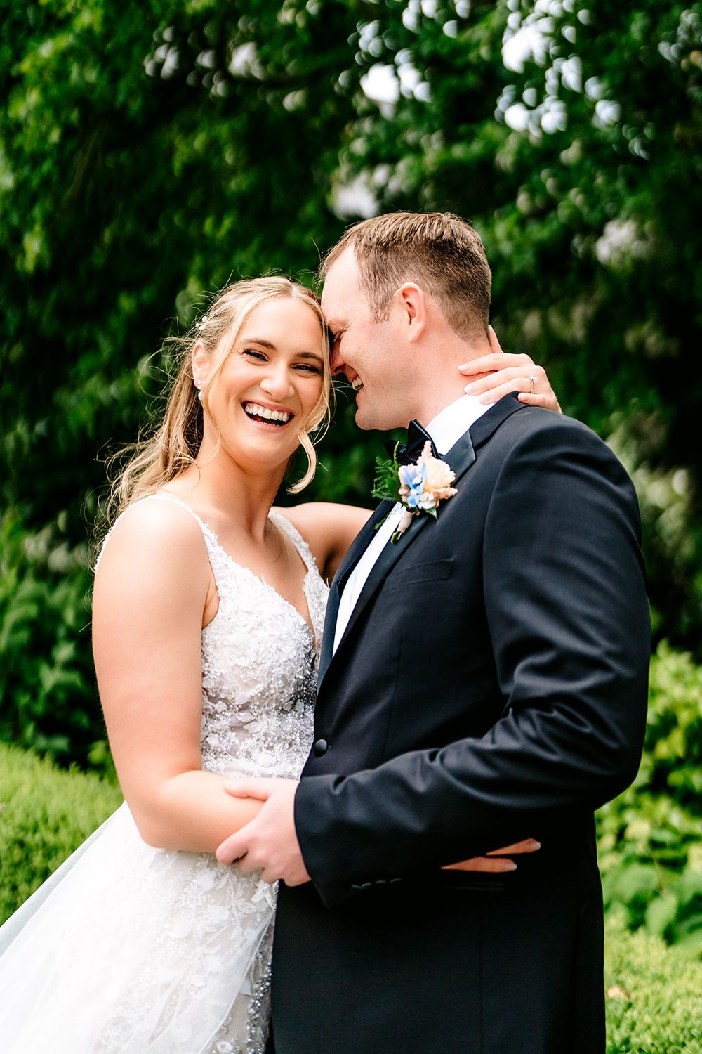 A couple shares intimate moments and laughter during their wedding photoshoot against a verdant garden backdrop.