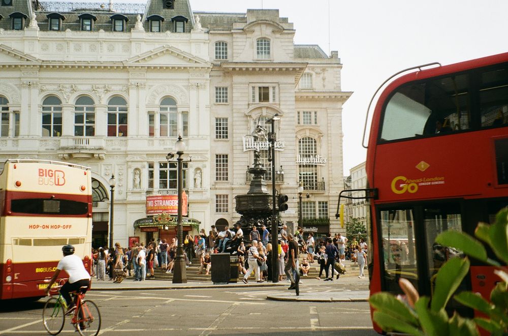 Iconic red double-decker bus and pedestrians at bustling Piccadilly Circus intersection in central London.