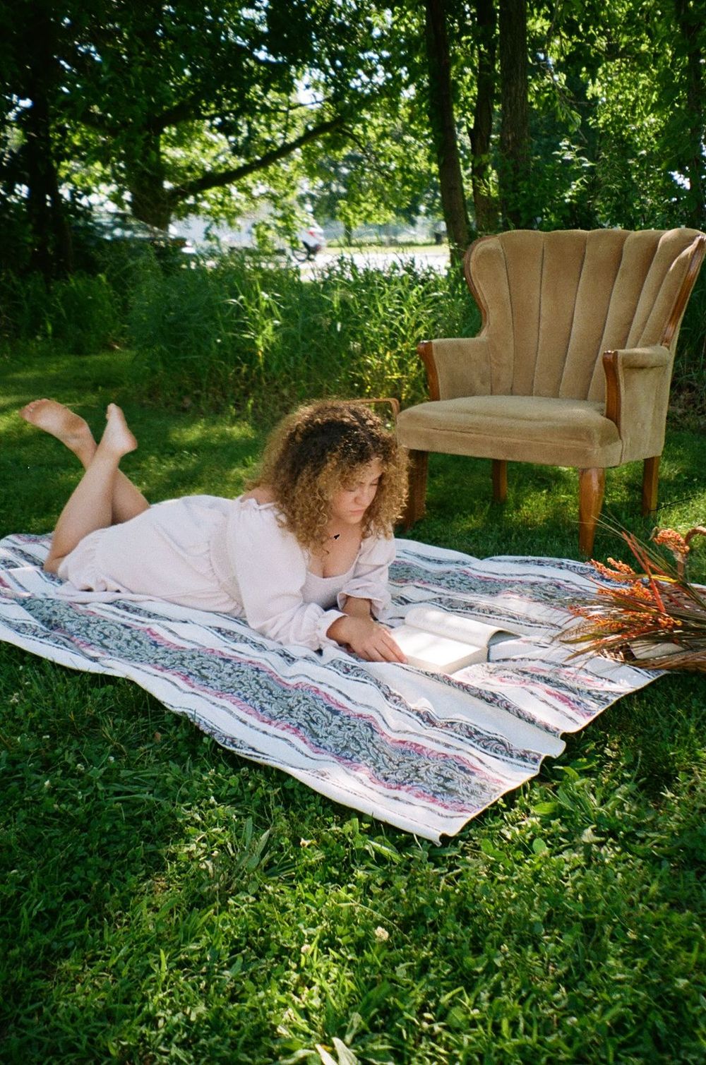 A soft velvet armchair sits on a patterned picnic blanket in a lush green garden setting during summer.