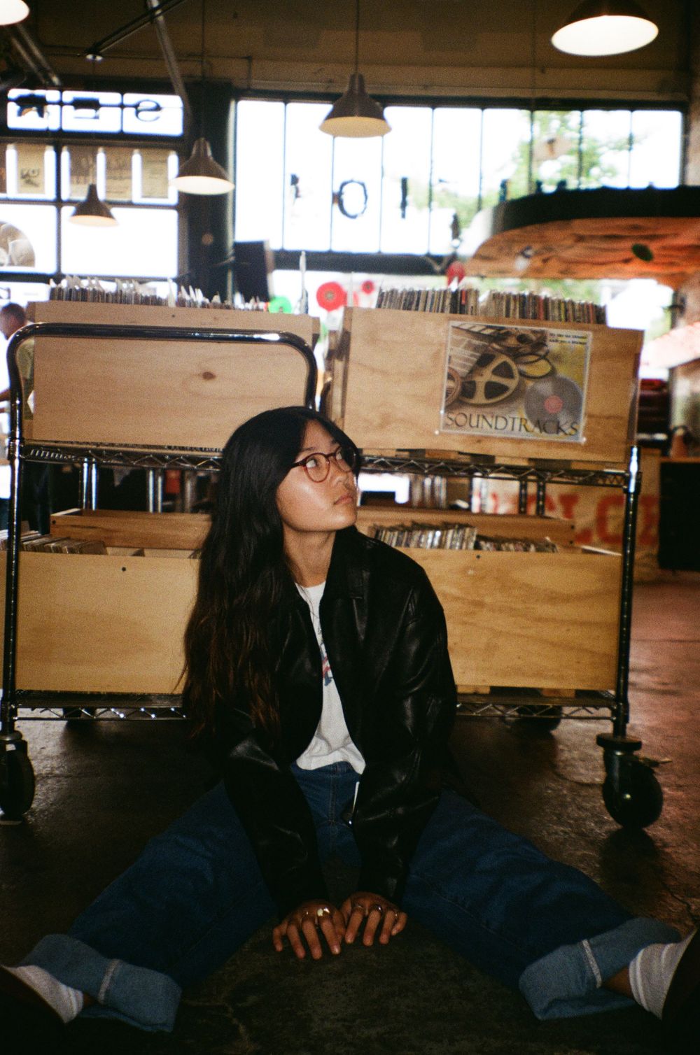 A vintage-style photo of someone sitting casually at a record store with wooden crates of vinyl albums.