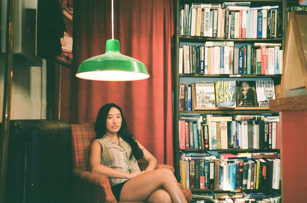 Someone sits in a cozy reading nook with bookshelves and a green pendant lamp in a vintage-style interior.