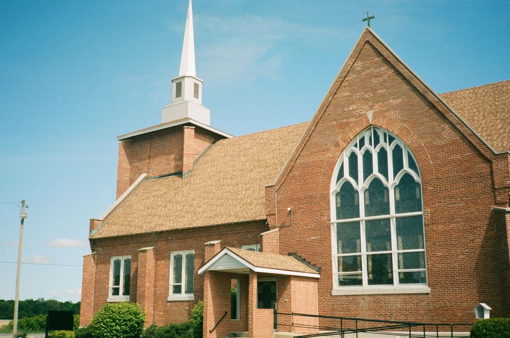 A brick church with gothic-style windows and a white steeple against a bright blue sky.